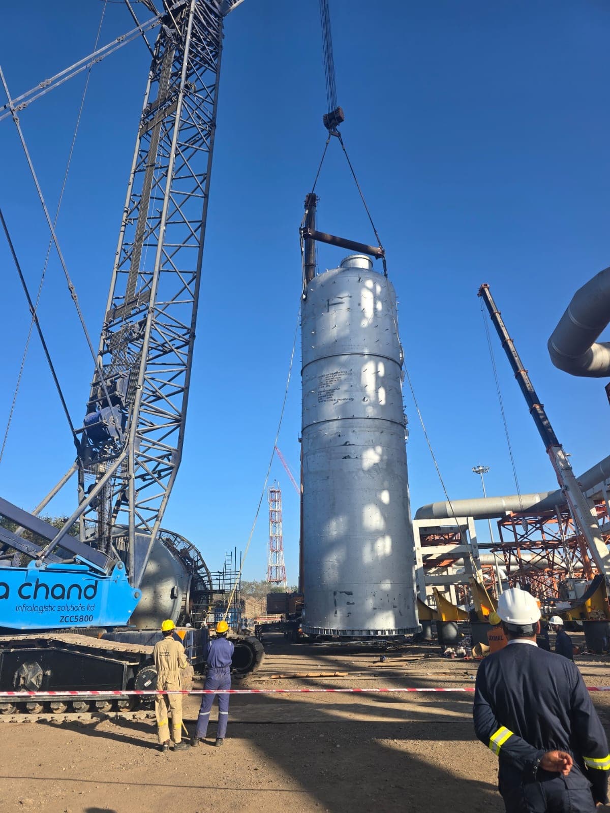 A tall process column being lifted into position by a crawler crane on a plant site