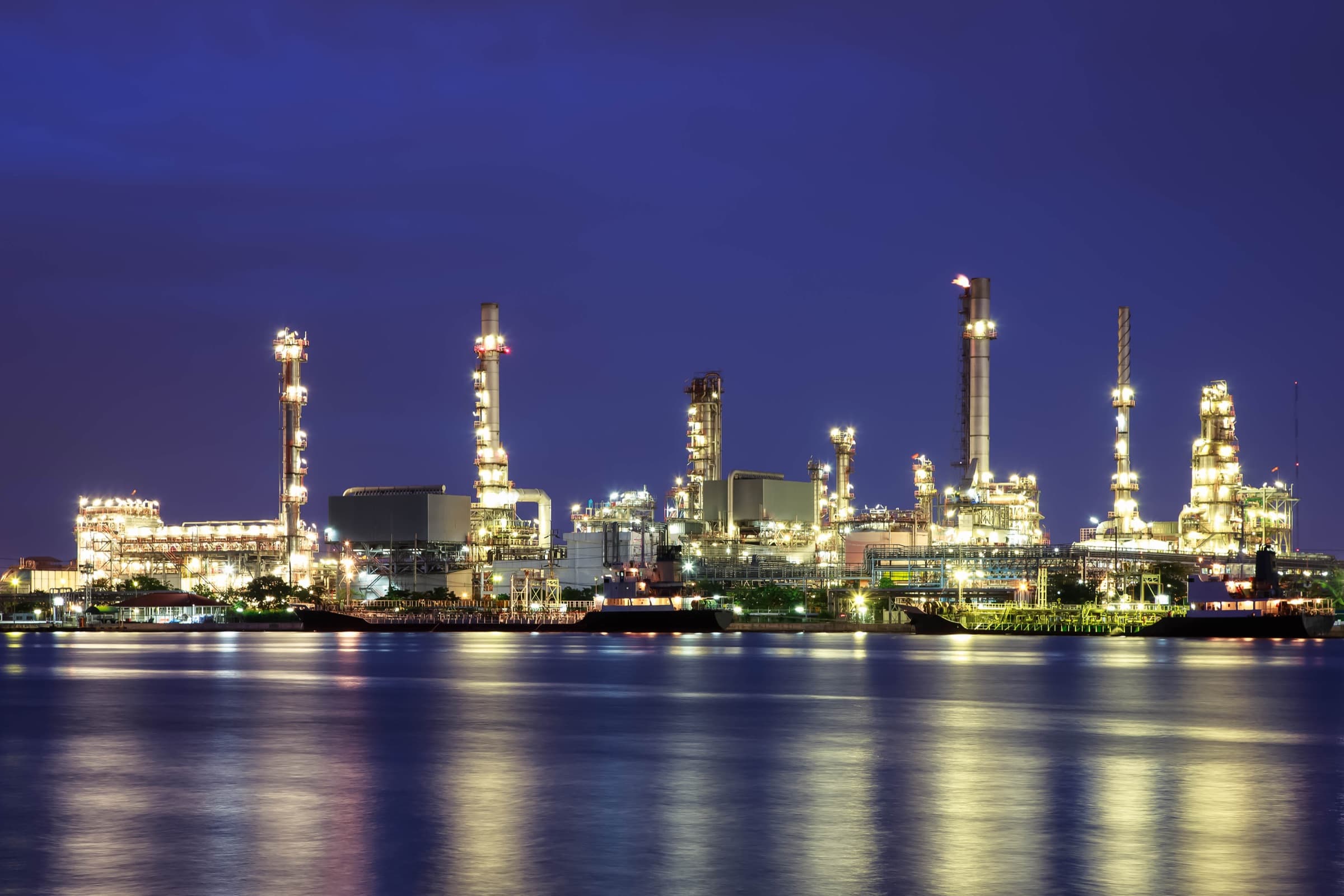 Illuminated refinery at dusk reflected on water